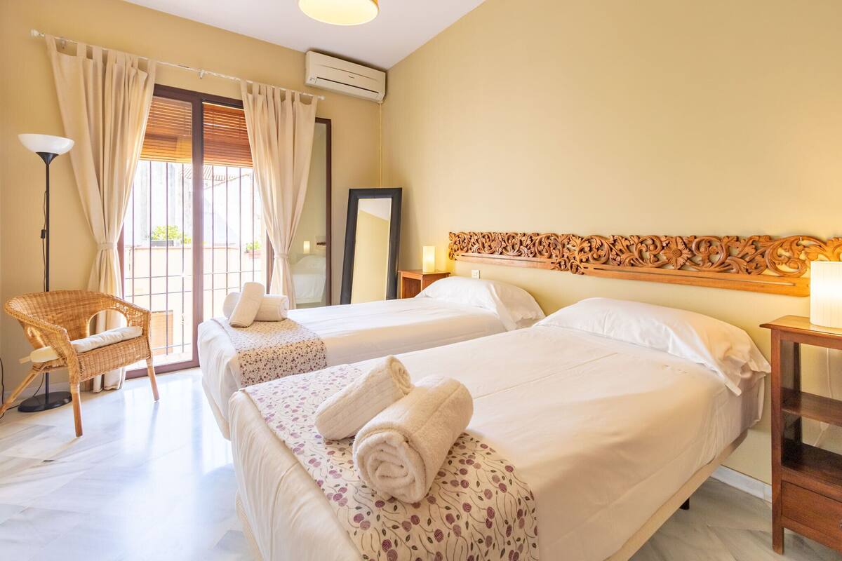 A hotel room with two beds, a wicker chair, a mirror, and a decorative wooden headboard.