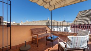 Una terraza con un banco de madera, sillas de mimbre y una mesa con una botella y un vaso.
