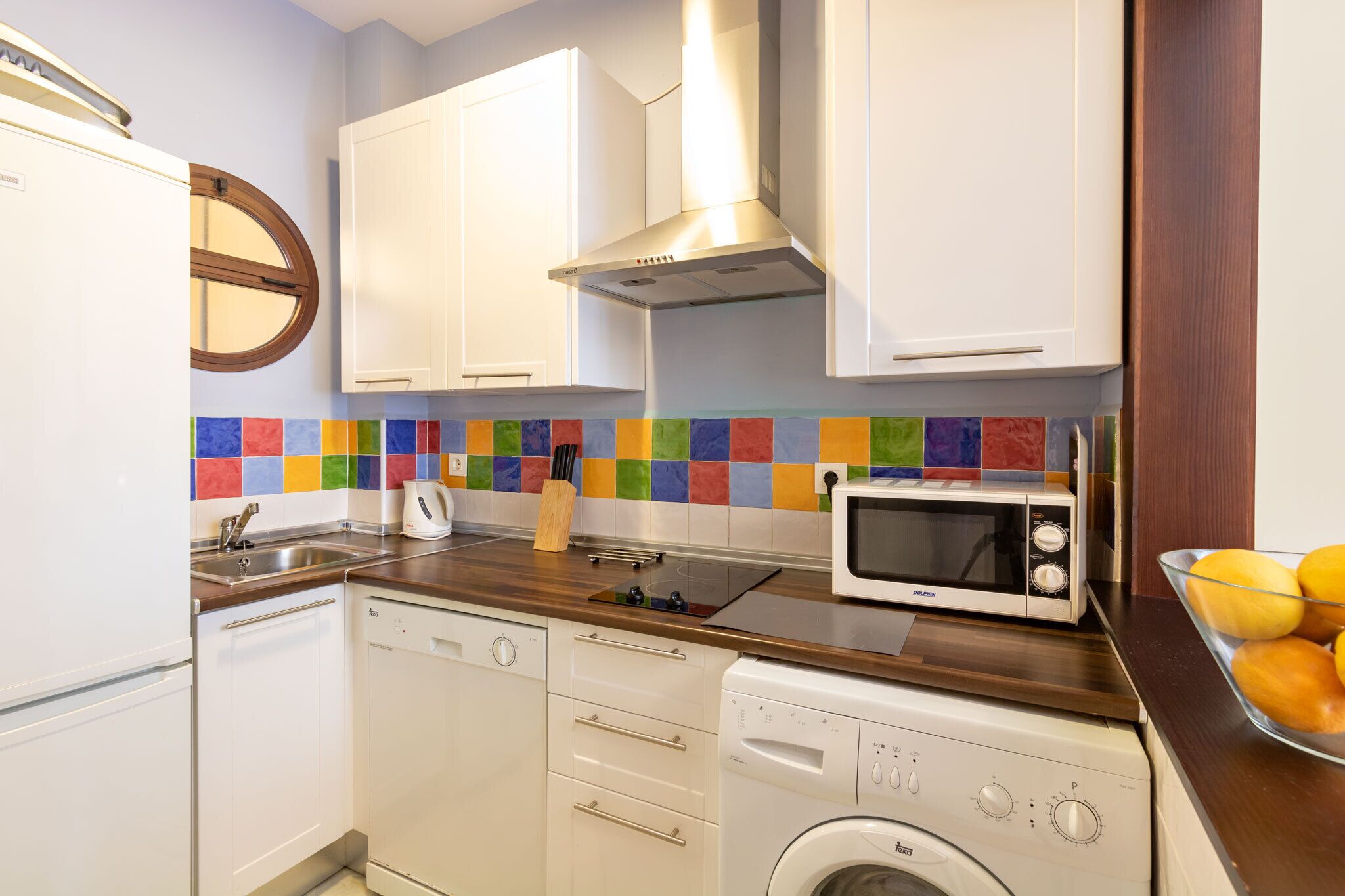 A compact kitchen with white cabinets, a microwave, a washing machine, and a dishwasher.