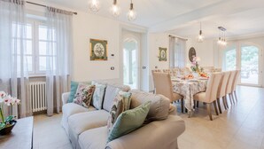 Een ruime woonkamer met een beige bank, een eethoek met een tafel voor vier personen en een uitzicht op de omgeving door grote ramen.