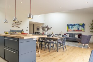 A modern kitchen with a central island, dining area with chairs, and a living room with a sofa and a painting.