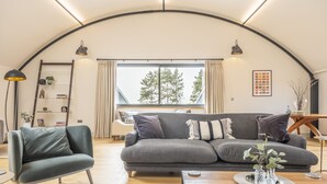 Een moderne woonkamer met een grijze bank, een houten salontafel en een ladderrek.