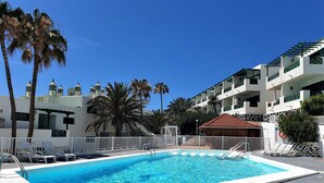 Une piscine entourée de chaises blanches, de palmiers et d’une clôture blanche.