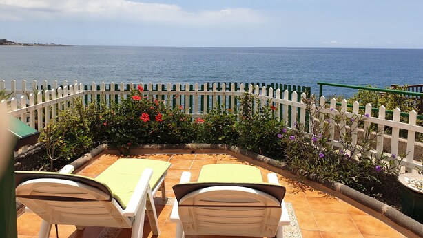 Une terrasse avec deux fauteuils et une clôture blanche en bois donnant sur la mer.