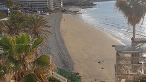 Une plage avec un bâtiment en arrière-plan, une clôture blanche et des palmiers.