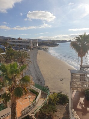 Una playa con un edificio al fondo, una cerca blanca y palmeras.