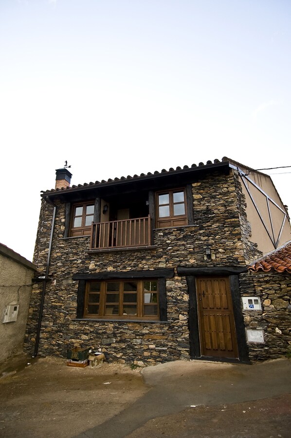 A two-story stone building with a balcony, wooden windows, and a brown door.