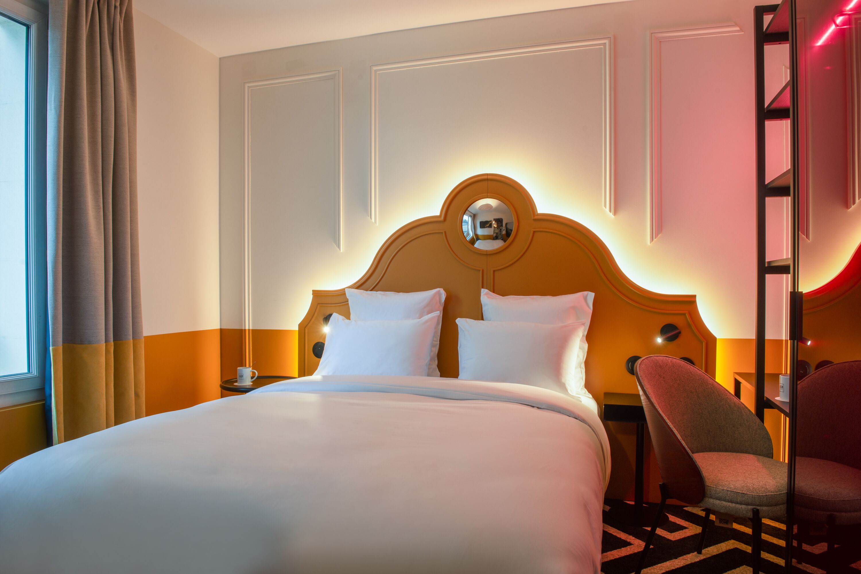 A hotel room with a large bed, a headboard with a mirror, a chair, and a nightstand.
