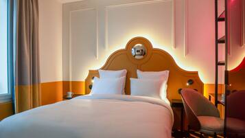 A hotel room with a large bed, a headboard with a mirror, a chair, and a nightstand.