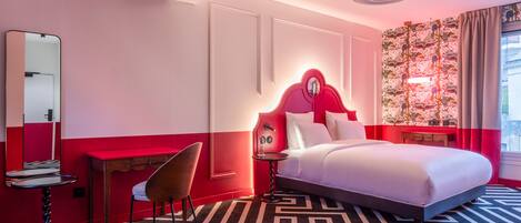 A hotel room with a bed, a desk, a chair, a mirror, and a patterned carpet.