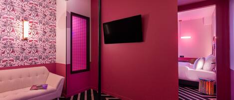 Ein Flur mit strukturiertem Wandpapier, einem weißen Sofa, einem Flachbildfernseher und einer rosa beleuchteten Tür.