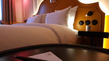 A hotel room with a bed, a bedside table with a pen and a notepad, and a lamp.