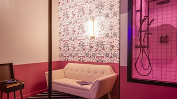 Una habitación con papel tapiz estampado, un sofá, una mesita con un tocadiscos y una ducha con pared iluminada en rosa.