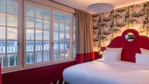 A hotel room with a large window, a red headboard, and a view of the cityscape. - LABE Hôtel Tours Centre Gare (Tours)