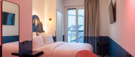 Habitación de hotel con cama, escritorio, silla, espejo, televisor y ventana con cortinas.