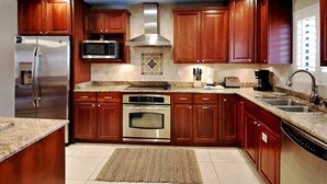 A modern kitchen with wooden cabinets, stainless steel appliances, and a granite countertop. - Aegean #329 | Community Pool & Tennis + Shuffleboard (Destin)