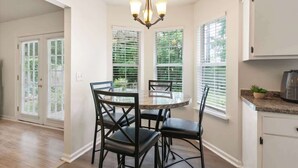 A dining area with a round table and four chairs, a chandelier, and a kitchen area with cabinets and a countertop. - Creekside Hideaway (Brunswick)
