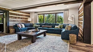Un salon moderne avec un canapé d’angle, une table basse et une grande fenêtre agrémentée de rideaux.