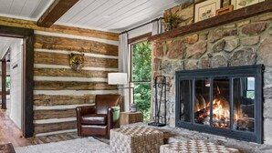 L’intérieur d’une cabane en rondins, avec une cheminée en pierre, un fauteuil en cuir et un pouf en osier tressé.