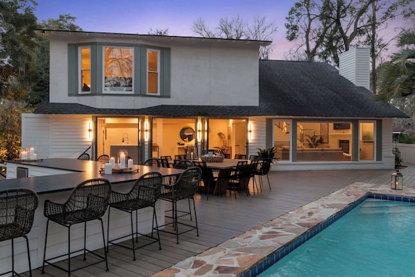 A modern house with a pool, outdoor dining area, and a fireplace. - 8BR Lakefront Estate | Pool, Hot Tub & Lake Access (Savannah)