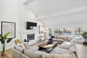 A spacious living room with a fireplace, large windows, and a view of an outdoor pool area.