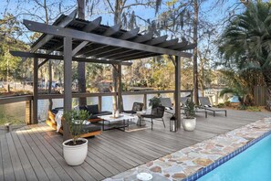 Eine Holzterrasse mit Sitzgelegenheiten im Freien, einem Pool und Blick auf einen See.