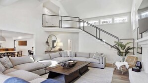 A spacious living room with a large sectional sofa, a coffee table, and a staircase leading to an upper level. - 8BR Lakefront Estate | Pool, Hot Tub & Lake Access (Savannah)