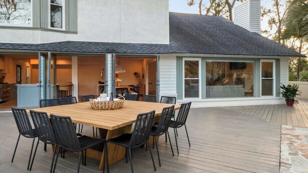 An outdoor dining area with a wooden table and black chairs, connected to a building with large windows and a stone pathway. - 8BR Lakefront Estate | Pool, Hot Tub & Lake Access (Savannah)