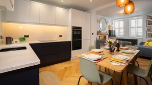 Eine moderne Küche mit weißen Schränken, einem eingebauten Backofen und einem Essbereich mit einem Holztisch für vier Personen.