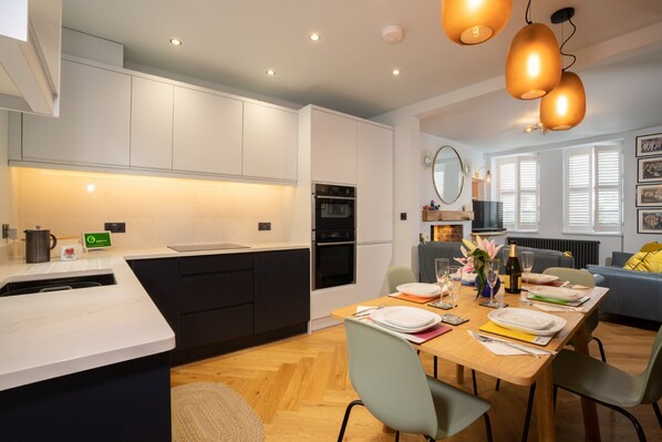 A modern kitchen with white cabinets, a built-in oven, and a dining area with a wooden table set for four.