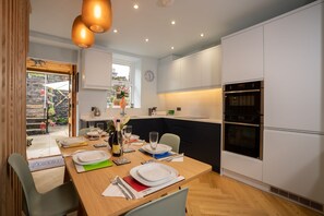 A modern kitchen with white cabinets, a built-in oven, and a dining area set for four with a wooden table and chairs.