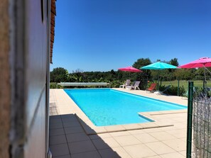 Una piscina con solárium de baldosas, rodeada de sillas de descanso y sombrillas.