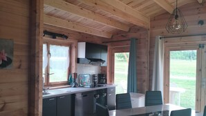 A wooden cabin interior with a kitchen, dining area, and a view of the outdoors.