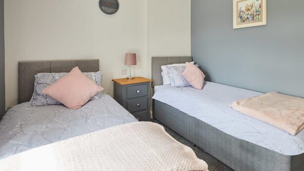 A bedroom with two beds, a bedside table, a lamp, a clock, and a framed picture on the wall. - Host & Stay | Castle View Cottage (Barnard Castle)