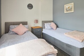 Une chambre avec deux lits, une table de chevet, une lampe, une horloge et un tableau encadré au mur.