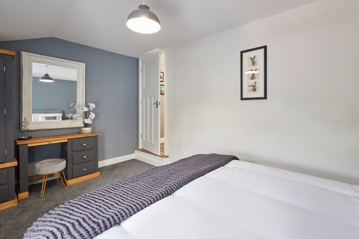 Un dormitorio con cama, escritorio, silla, cómoda, espejo y puerta.