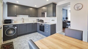 A modern kitchen with grey cabinets, a wooden dining table, and a built-in washing machine. - Host & Stay | Castle View Cottage (Barnard Castle)