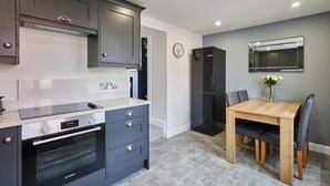 A modern kitchen with dark cabinetry, a Bosch oven, a black refrigerator, and a wooden dining table with chairs. - Host & Stay | Castle View Cottage (Barnard Castle)