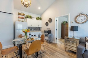Une cuisine moderne avec des meubles blancs, un réfrigérateur et un coin repas comprenant une table et des chaises en verre.