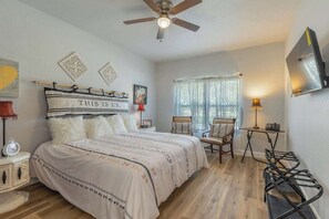 A bedroom with a bed, a chair, a desk, a ceiling fan, and a window with curtains.