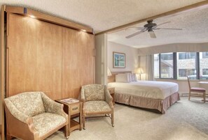 A hotel room with a bed, two armchairs, a nightstand, a ceiling fan, and a window with a view. - Grand Lodge Studio | Walk to Crested Butte Lifts, Pool, Hot Tub, Dog-Friendly (Crested Butte)