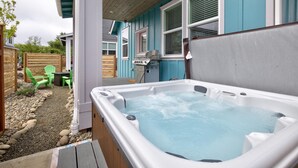 A hot tub in a backyard with a wooden deck, a barbecue grill, and green chairs.
