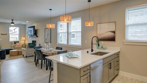 A modern kitchen with a central island, pendant lighting, and a view of the living area.