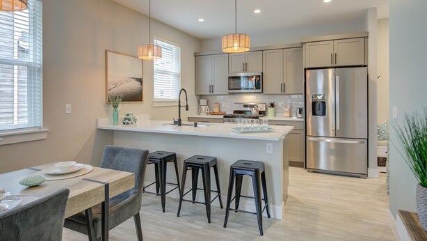 A modern kitchen with a central island, stainless steel appliances, pendant lighting, and a dining area with bar stools.