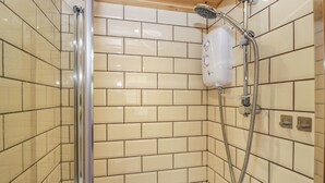 A shower area with a glass door, a handheld showerhead, and a wall-mounted control panel. - Rabbit Hill Hut (Abergavenny)