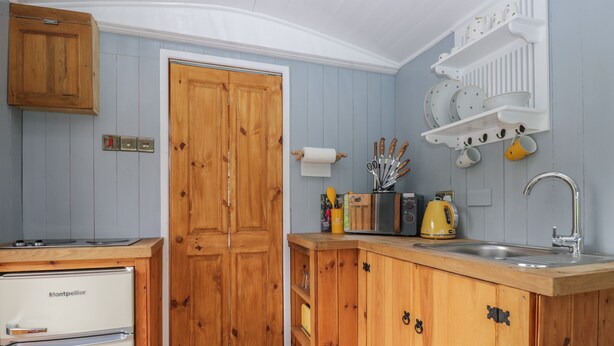 A compact kitchen with wooden cabinets, a built-in stove, a sink, and a microwave. - Rabbit Hill Hut (Abergavenny)