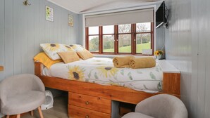 A bedroom with a wooden bed, a bedside table, a chair, and a window with a view of the outdoors. - Rabbit Hill Hut (Abergavenny)