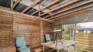 A rustic wooden cabin with a telescope on a table, two chairs, and a bench. - Rabbit Hill Hut (Abergavenny)