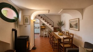 A cozy interior with a dining area, a fireplace, and a staircase leading to a kitchen. - AMORE RENTALS - Casa Laura with Sea View Terrace (Positano)