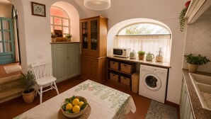 A compact kitchen with a washing machine, microwave, and wooden cabinets. - AMORE RENTALS - Casa Laura with Sea View Terrace (Positano)